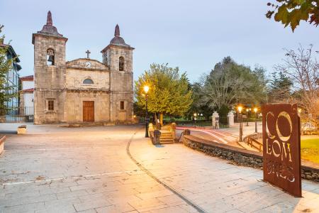 Facade of a stone church with two bell towers in a square with trees
