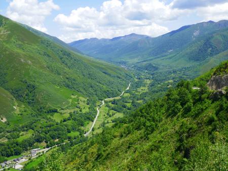 A mountain road winds through a lush valley between forested mountains