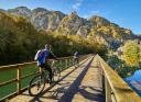 Two cyclists crossing a long wooden bridge over a reservoir