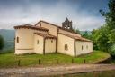 Rural stone church surrounded by green meadows, trees and mountains