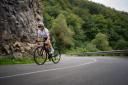 A female cyclist climbing a mountain road with trees in the background