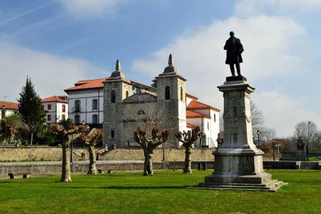 Fachada de una iglesia de piedra con dos campanarios en una plaza con árboles