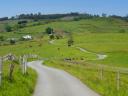 A rural road winds between green hills and meadows with country houses