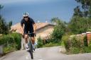A cyclist climbs a hill with a chalet and a rural landscape in the background