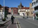 A cyclist pedals through the city's historic center with a Gothic collegiate church in the background
