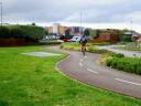 A cyclist on the Gijón bike lane, crossing a green area with buildings in the background
