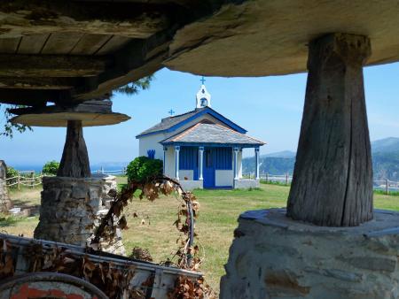 A white and blue hermitage on a cliff, with a traditional granary and sea views