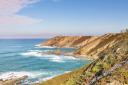 Spectacular aerial view of rugged coastal cliffs and a lighthouse in the background