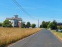 An asphalt road runs between cultivated fields and a distant church