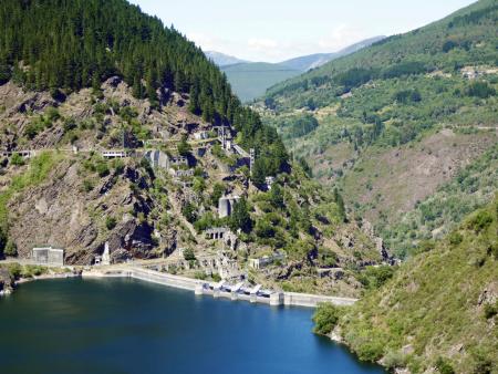 Aerial view of a blue-green reservoir and a dam surrounded by high mountains and vegetation