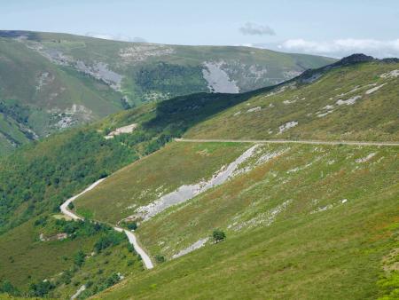 A mountain road winds its way up a large green hillside