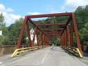 A road crosses the river over a red metal bridge in a forest area