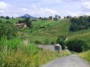 A rural landscape of green hills with trees, houses, and a winding road