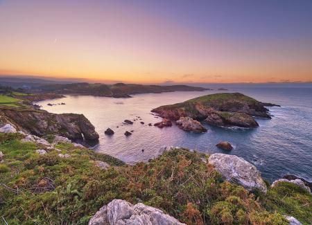 Sunset over a coastal reserve with a rocky islet in front of the bay