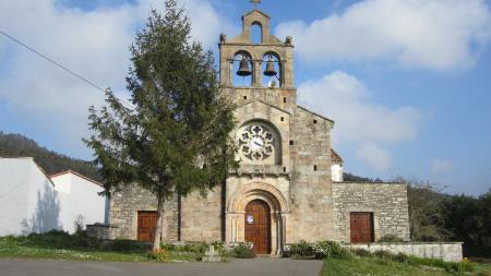 Facade of an old stone church with a belfry, two bells and a tree in front