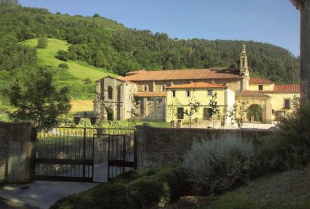 Old monastery with an iron gate surrounded by green fields and hills
