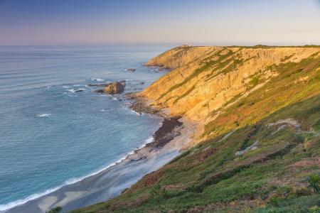 Spectacular aerial view of rugged coastal cliffs and a lighthouse in the background