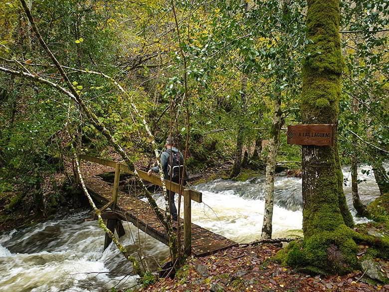 Section of the road to the glacial lagoons where a man is crossing a wooden bridge over the river and the signpost to the lagoons can be seen.
