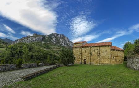 Stone Romanesque church in a meadow with mountains and trees in the background