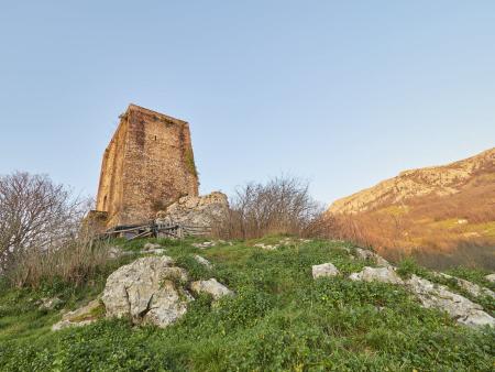 Old stone tower on a hill seen from below with mountains behind