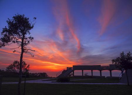 Un atardecer con un cielo rojo, naranja y azul sobre un mirador junto al mar