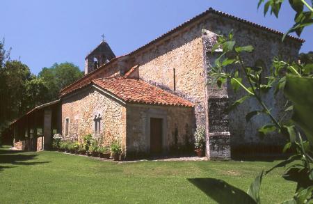 A Romanesque stone church with a portico and a tiled roof in a meadow