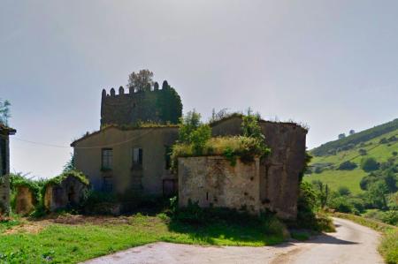 A ruined stone house with a medieval tower next to a road
