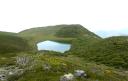 A serene mountain lake surrounded by green peaks under a cloudless sky
