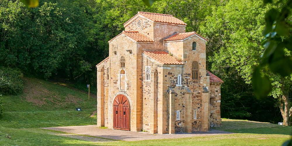 The iconic façade of the church of San Miguel de Lillo in Asturias, highlighting its unique architecture and surrounded by greenery.
