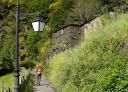 Hiker walking through the village of Ferreira, between slate houses and vegetation.