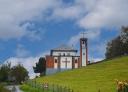 Ponticiella church with white façade and cross on a sloping meadow.