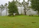 Recreational area with wooden benches among trees and mist in Boal