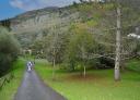 Cyclist on asphalt path between trees and mountains in Mier