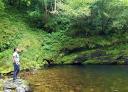 Young man by a clear pool in a green and rocky environment