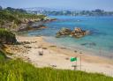 Arnao beach with golden sand, rocks and bathers on the shore.