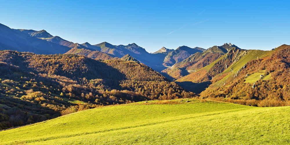 Vista de la autopista del Huerna desde la carretera del puerto de Pajares, en Lena, con un prado de verde intenso en primer plano y montañas al fondo.