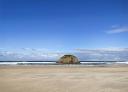 View of the sea from a sandy beach with a large rock in the background.