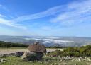 Several rocks piled up on a path with the mountains and a sea of clouds in the background.