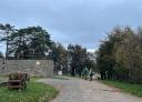 Couple of hikers on a tree-lined asphalt path near a stone building.