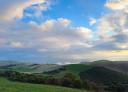 Wide panoramic view of green meadows and forests under a blue sky with clouds