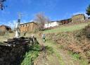 Hiker ascending a rural dirt road near stone houses.
