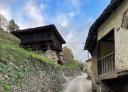 Road with a stone wall and a granary on the left and stone houses on the right.