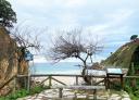 Viewpoint overlooking the beach with wooden railing, wooden bench, information sign and sea view.
