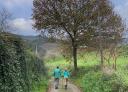 Couple of hikers on an asphalted stretch, surrounded by green vegetation.