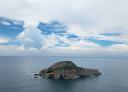 Rocky island in the sea under a blue sky dotted with white clouds