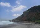 Beach with rocky coastline and calm sea under a partly cloudy blue sky