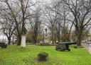 Ancient cannon and metal sculptures in a tree-lined urban park with green lawns
