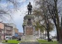 Bronze statue of a man standing on a pedestal, surrounded by trees.