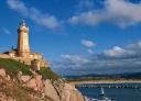 Lighthouse on a rocky cliff with a blue sea with several ships and a cloudy sky.