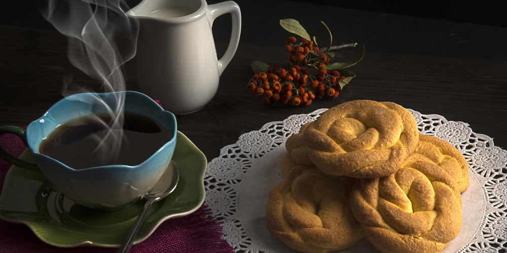 Marañuelas sobre una mesa acompañadas de una taza de café humeante y una jarrita de porcelana blanca con leche, sobre fondo negro.